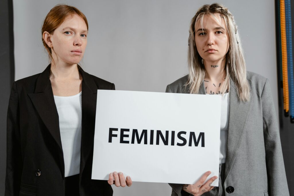 Two women in blazers holding a sign advocating feminism and empowerment.