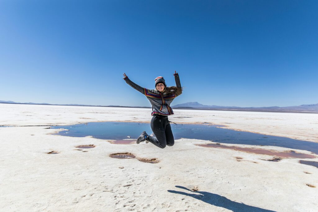 Smiling woman jumps with joy at Bolivia's Uyuni Salt Flats under a clear blue sky.