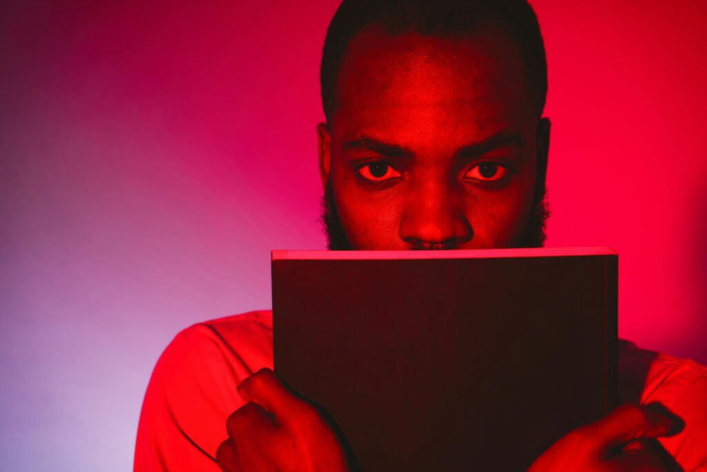 Close-up portrait of a man with a book, featuring dramatic red lighting and a mysterious mood.