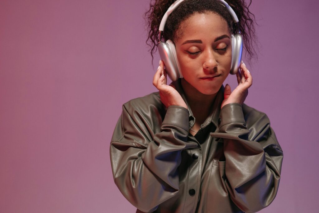A woman in a gray leather jacket enjoys music with her eyes closed and headphones.