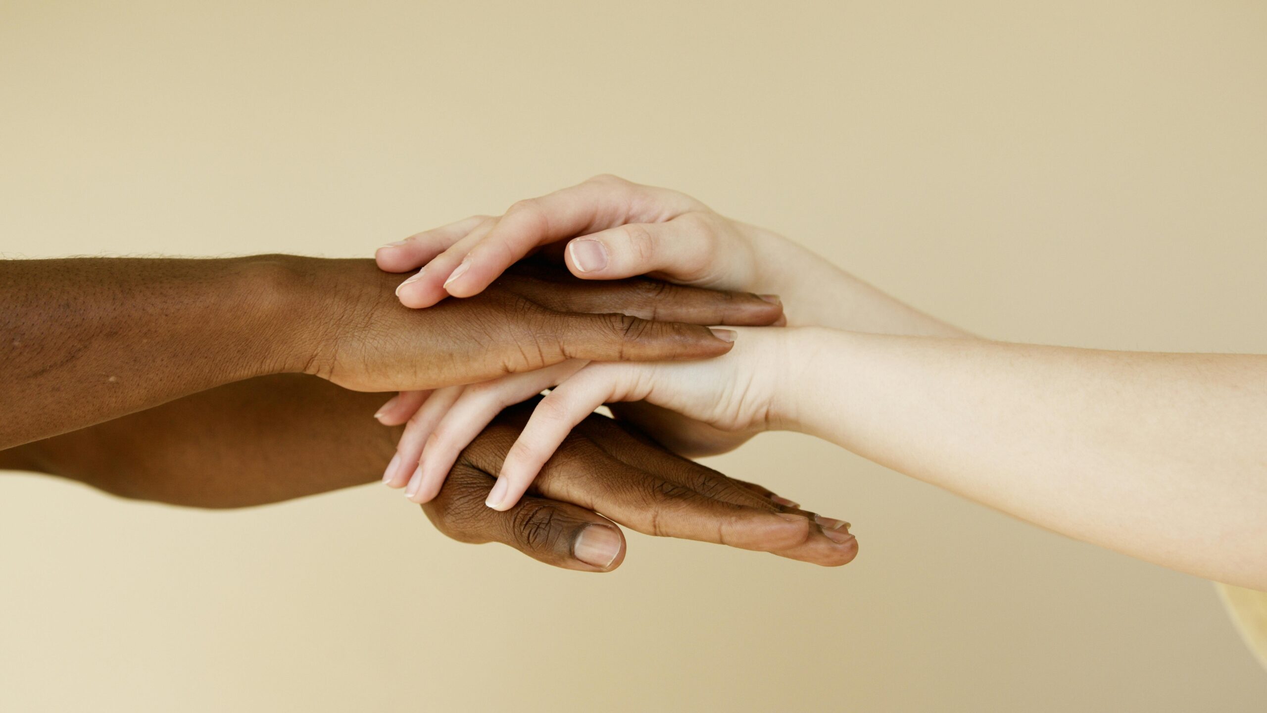 Close-up of diverse hands intertwined symbolizing unity and cooperation on a neutral background.