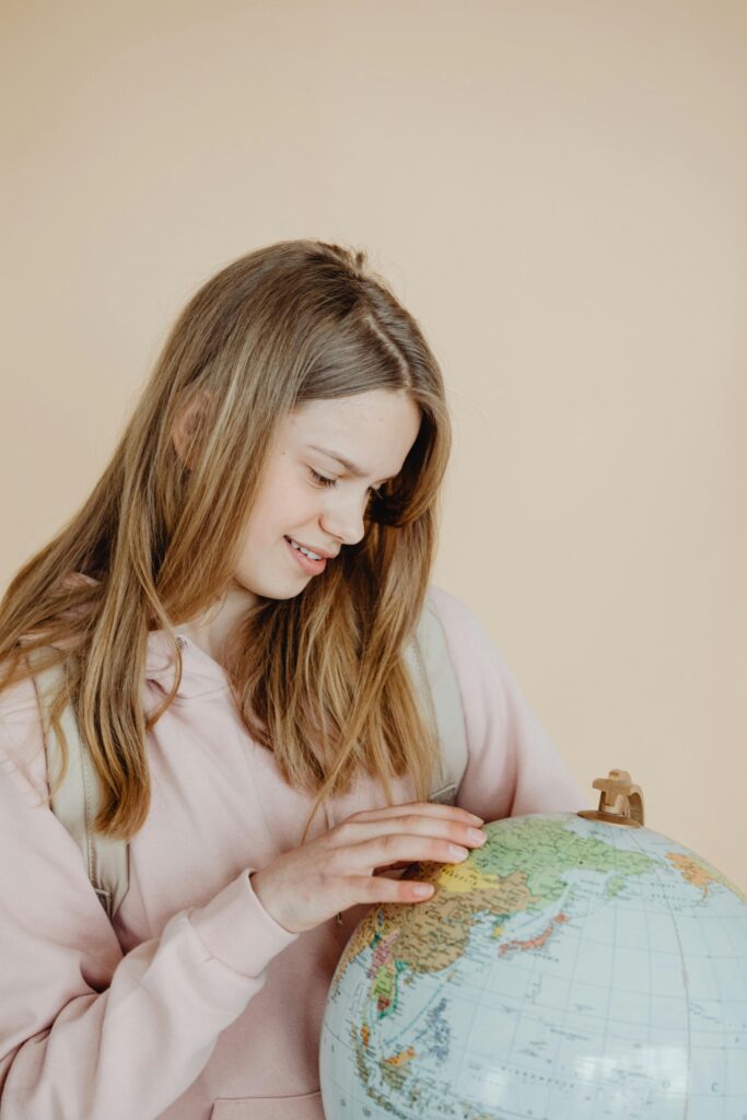 Smiling teenage girl examining a world globe in a pink sweater.