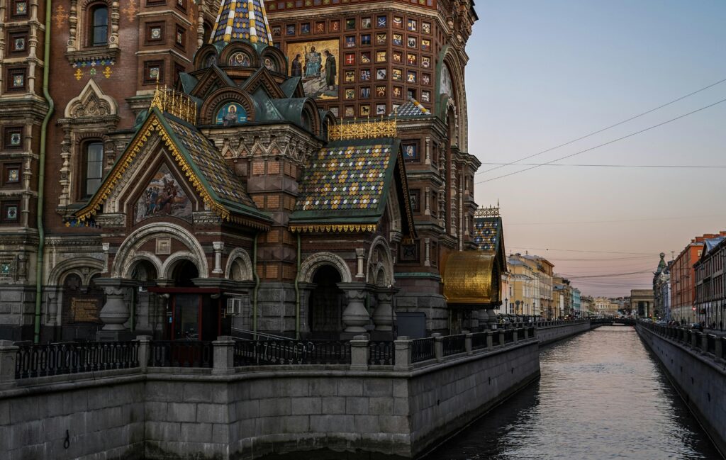 Beautiful church with colorful domes beside a canal in St. Petersburg during sunset.
