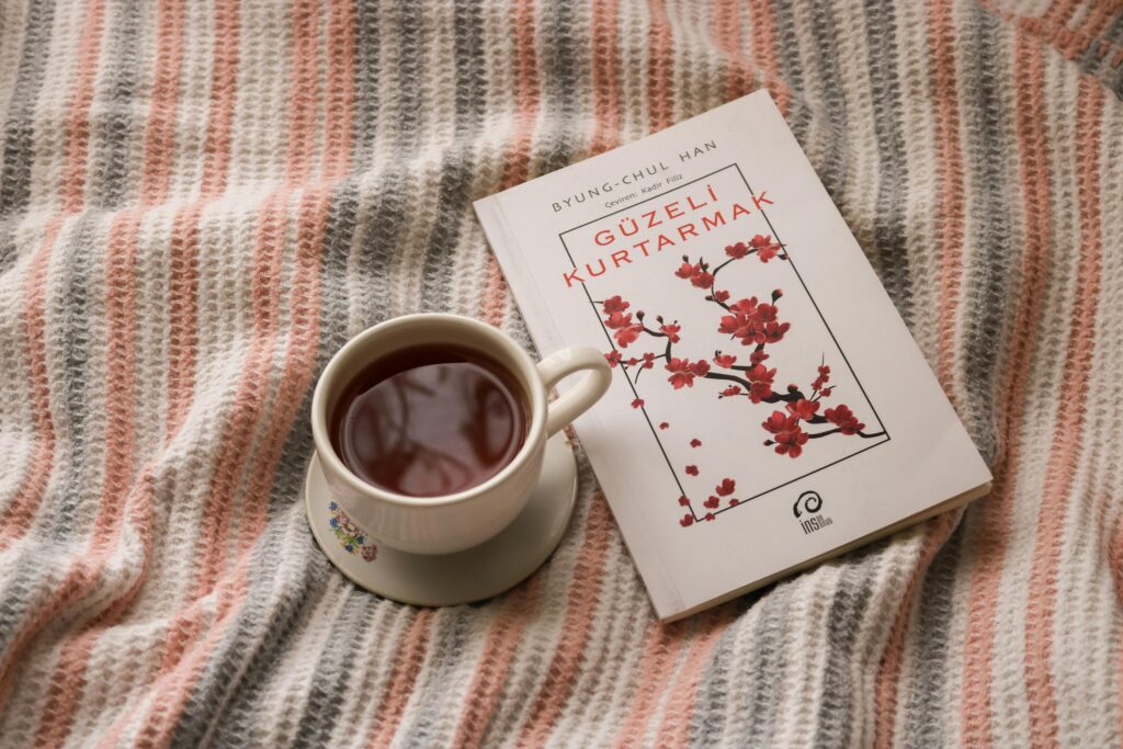 A steaming cup of tea beside a book on a warm, striped blanket, creating a cozy ambiance.