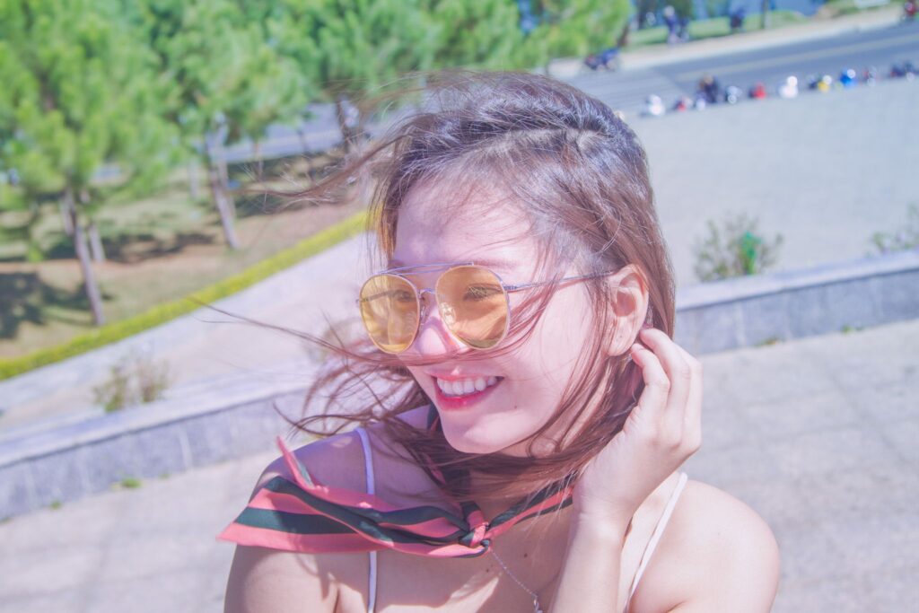 Joyful portrait of a young woman wearing sunglasses in a sunny Vietnamese park.