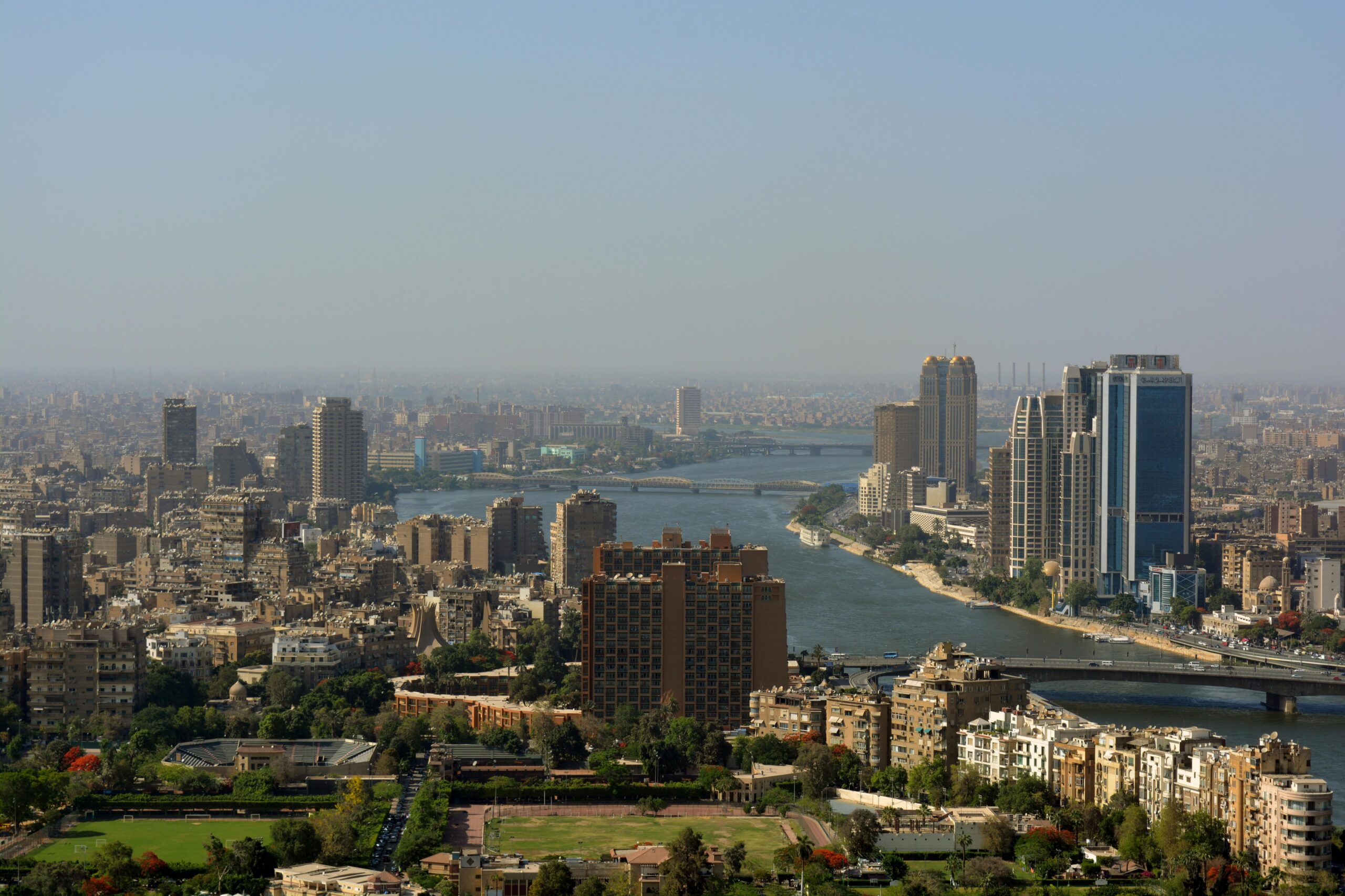 Aerial panorama of Cairo cityscape featuring modern skyscrapers and the Nile River.