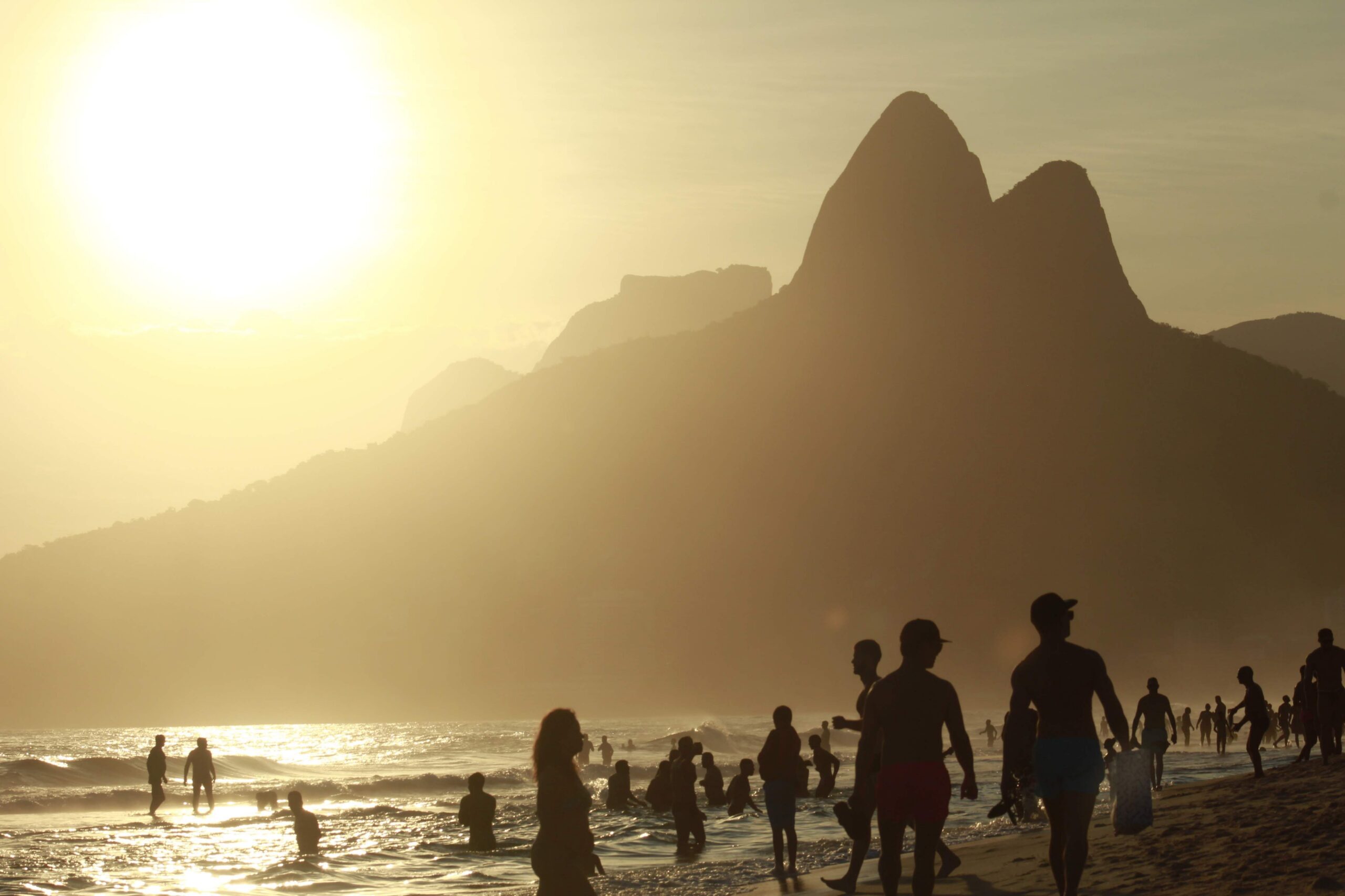 Silhouettes of people enjoying a stunning sunset at a scenic beach with mountain views.
