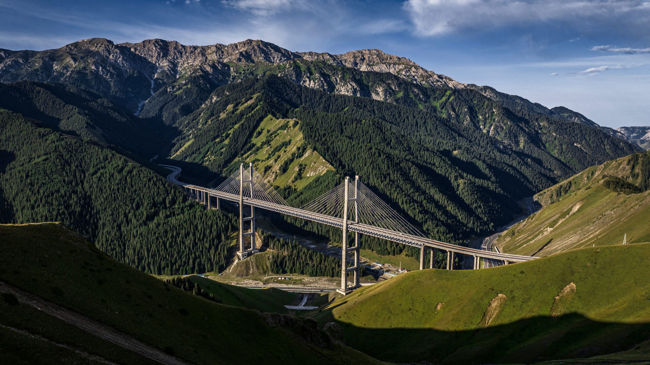 Scenic aerial view of the Guozigou Bridge amidst lush greenery and mountains in Xinjiang, China.