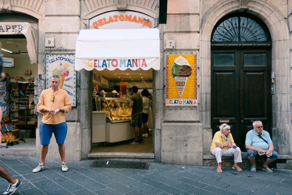 Street scene with Gelato shop entrance, people relaxing outside, a vibrant ice cream display.