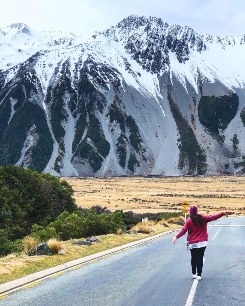 A woman walks along a road with stunning snow-capped mountain backdrop in New Zealand's Canterbury region.