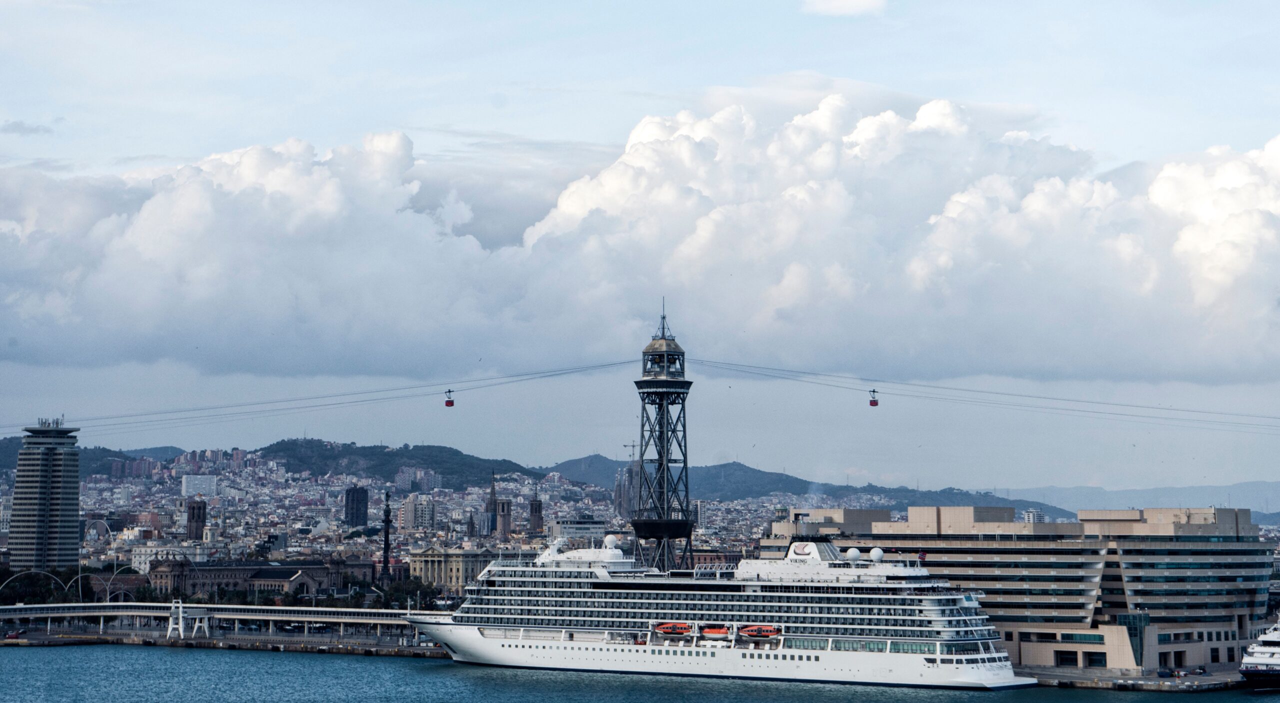 Stunning view of Barcelona harbor with a cruise ship and city skyline under dramatic clouds.