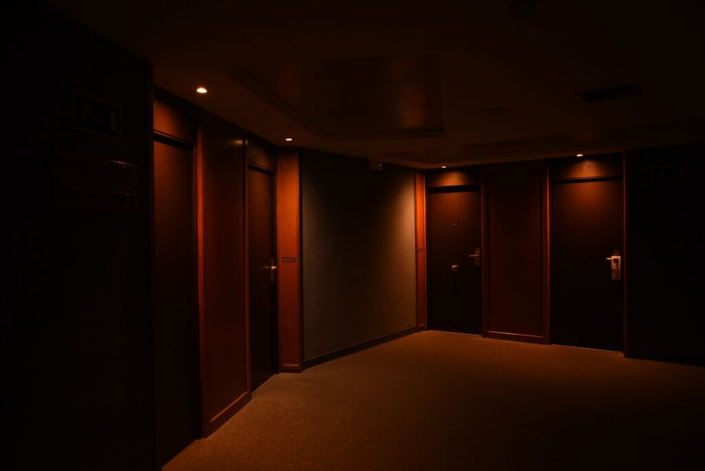 A dark, quiet hotel corridor featuring multiple closed wooden doors and soft lighting.