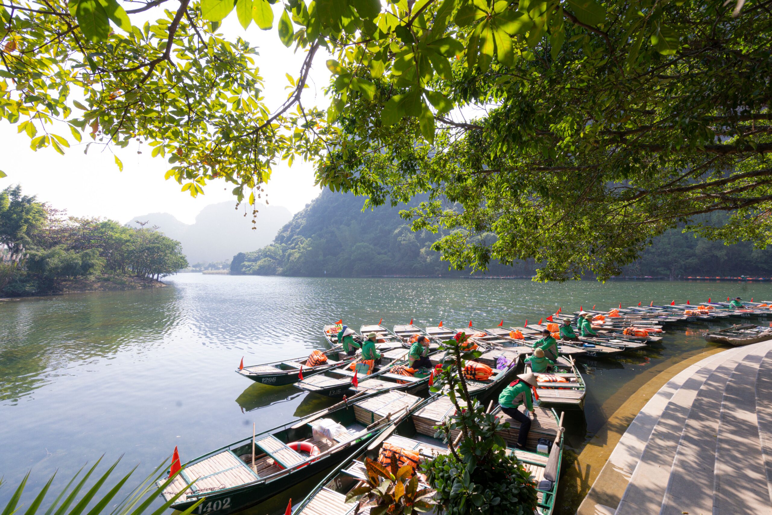 Peaceful scene of docked boats along the riverbank surrounded by lush greenery in Ninh Bình, Vietnam.