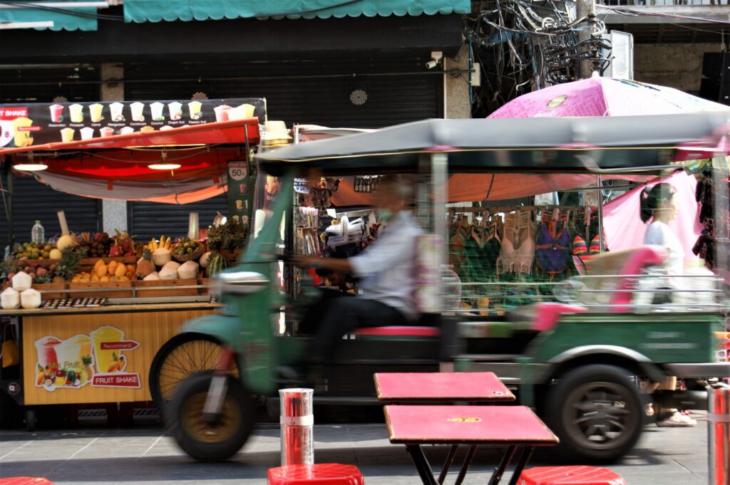 Vibrant street scene in Bangkok showcasing a moving tuk tuk and colorful market stalls.