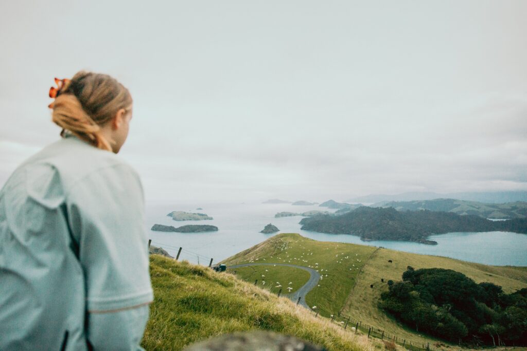 A woman gazes over the picturesque greenery and ocean of Coromandel, New Zealand.