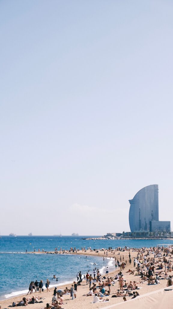 Crowded beach scene in Barcelona, Spain with clear skies and a view of the ocean.