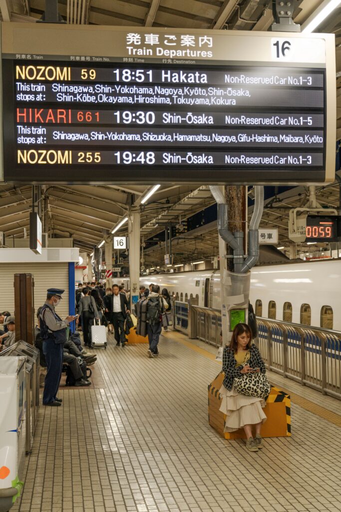 Commuters on a train platform in Japan with electronic departure board.