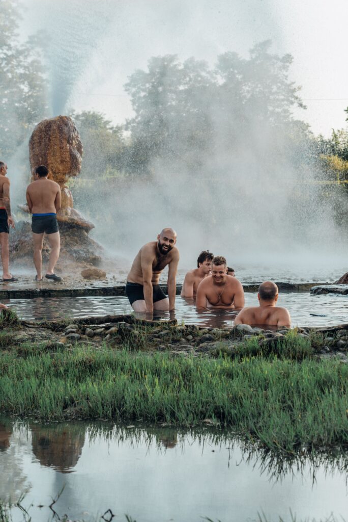 Group enjoying natural hot springs at day with steam rising outdoors.