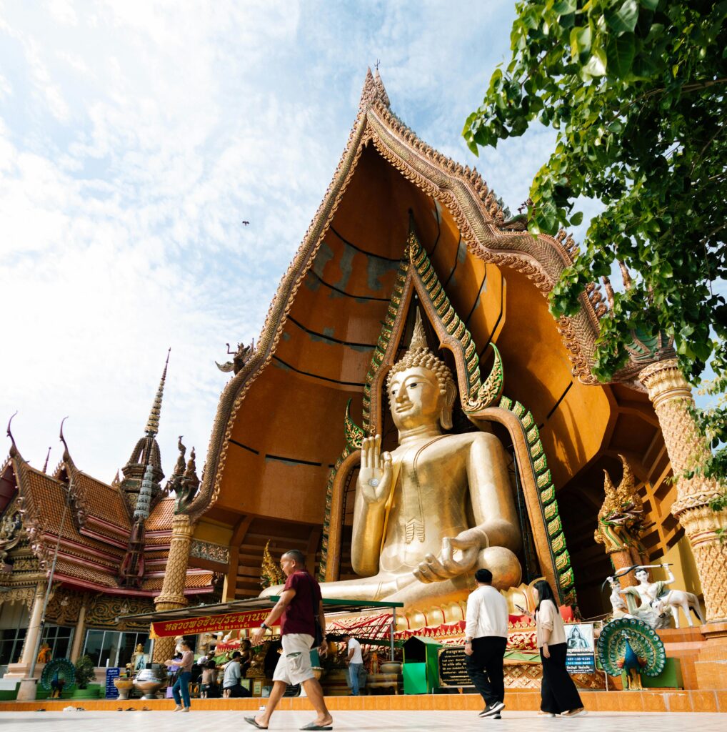 A magnificent golden Buddha statue at Wat Tham Sua in Kanchanaburi, Thailand, under a clear sky.