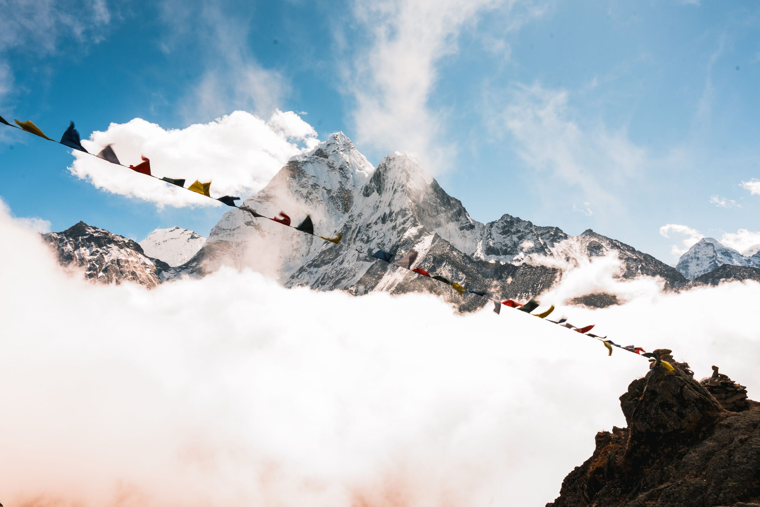 Majestic Himalayan peaks rise through the clouds with colorful prayer flags in the foreground, capturing the essence of Nepal's beauty.