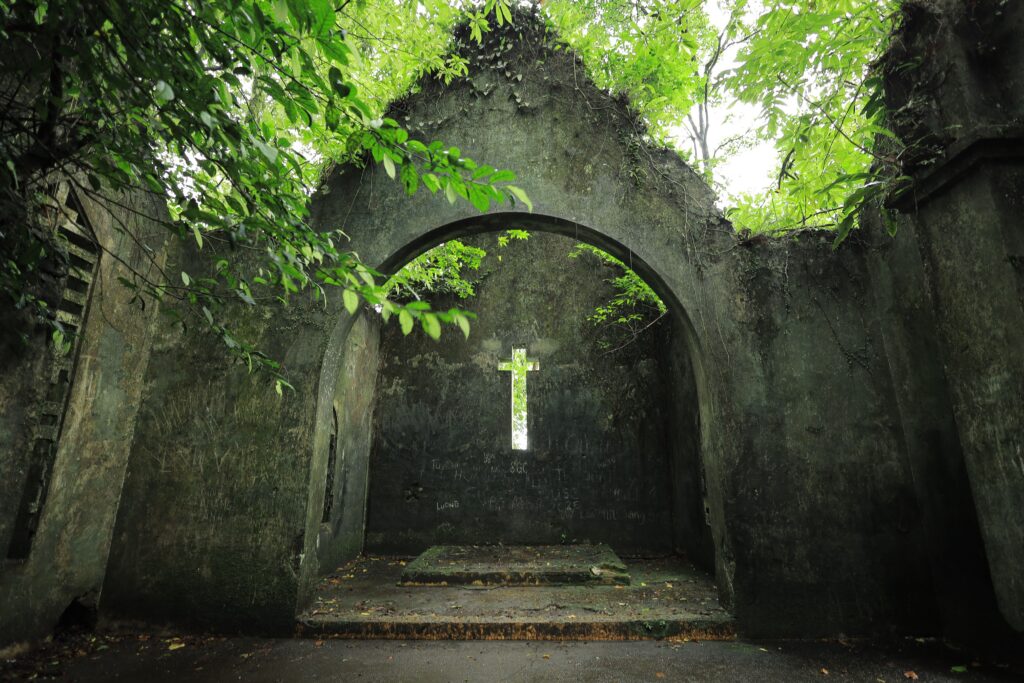 Ancient stone archway with a cross, surrounded by lush green foliage in Vietnam.
