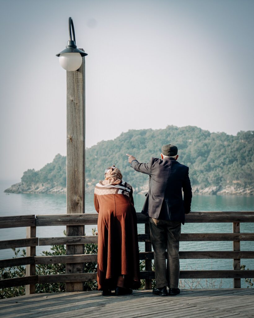 Senior couple on a wooden deck gazing at the ocean, a peaceful moment captured by the sea.