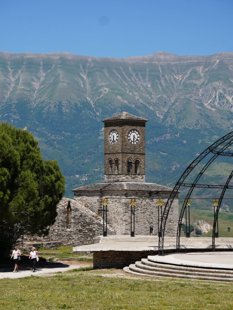 Stone clock tower with mountain backdrop in Gjirokastër, Albania.