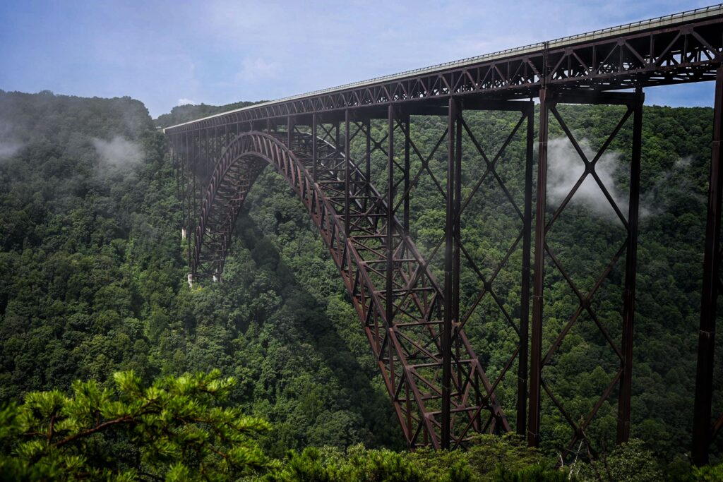 A breathtaking view of the New River Gorge Bridge surrounded by lush summer greenery and mist.