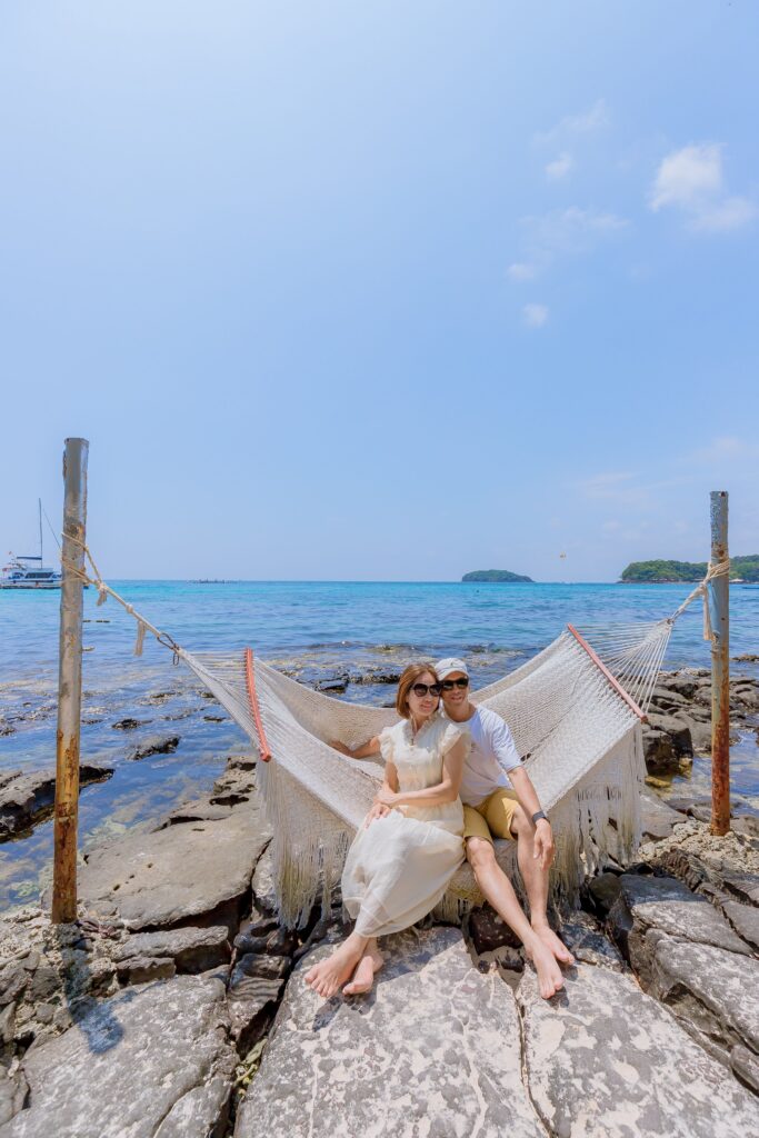 A couple enjoys a peaceful moment on a hammock by the ocean on a sunny day.