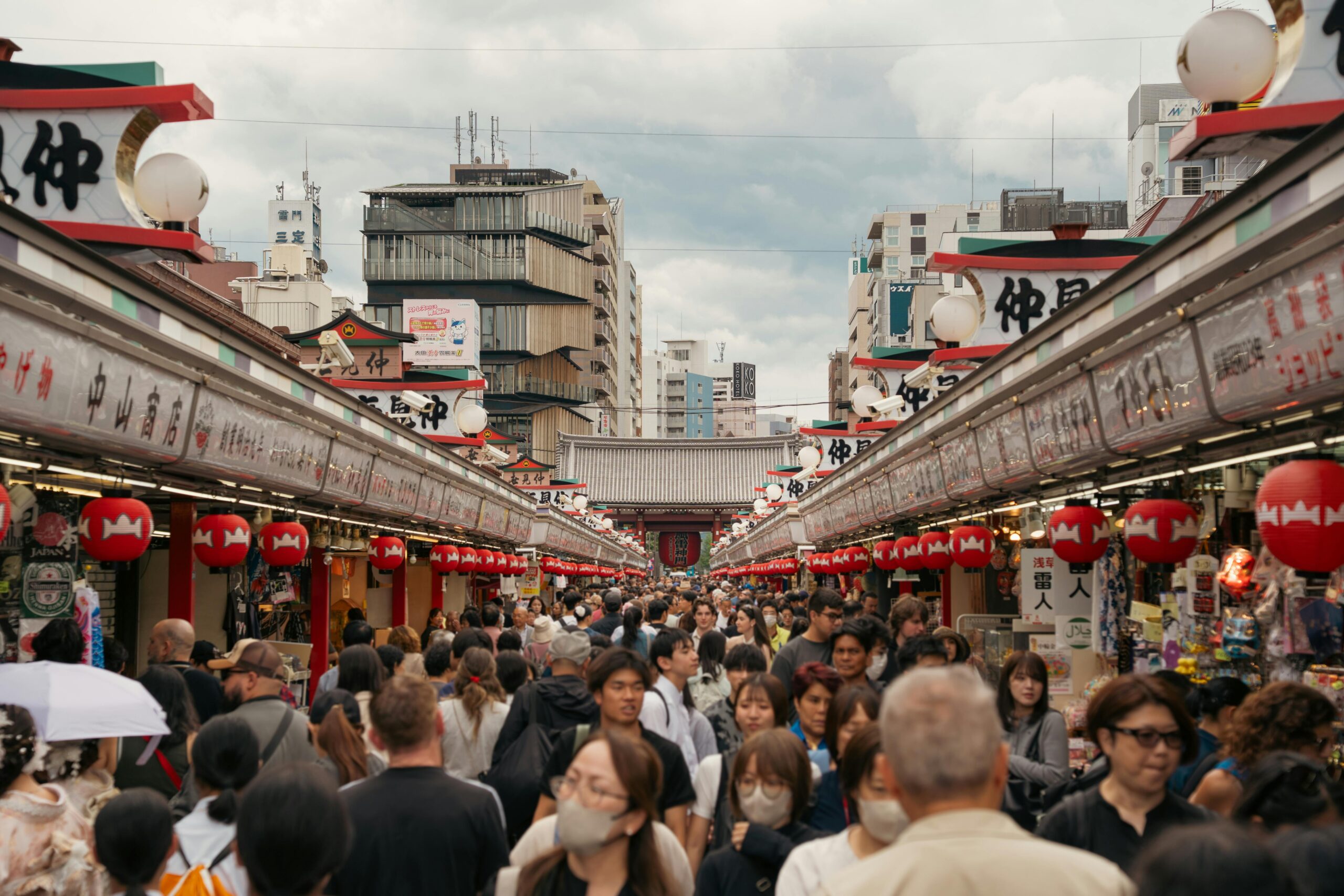 Vibrant street market in Asakusa, Tokyo with red lanterns and bustling crowd.