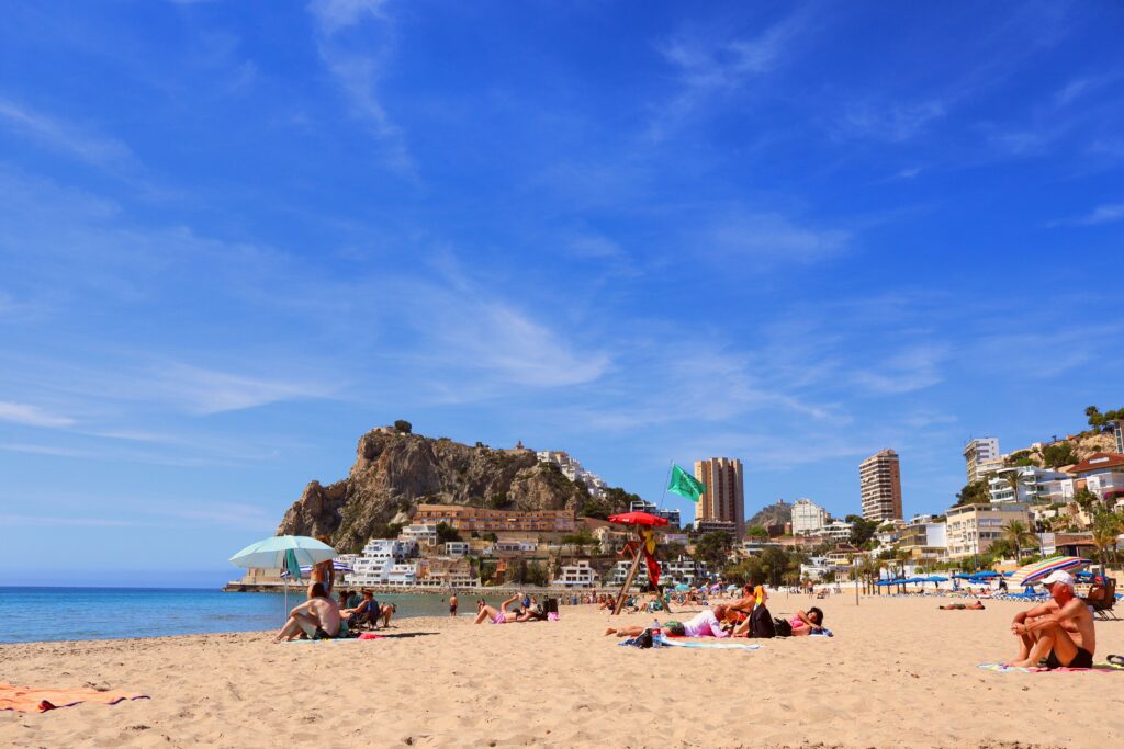Relaxing beach in Alicante, vibrant day with clear blue skies and bustling city backdrop.
