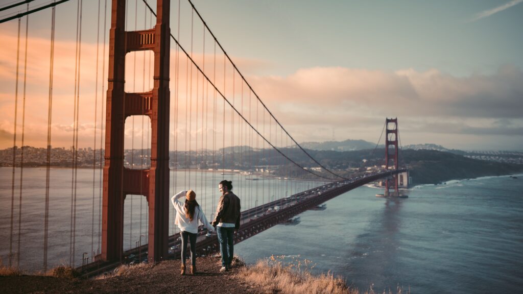 A couple embraces while overlooking the Golden Gate Bridge at sunrise in San Francisco.