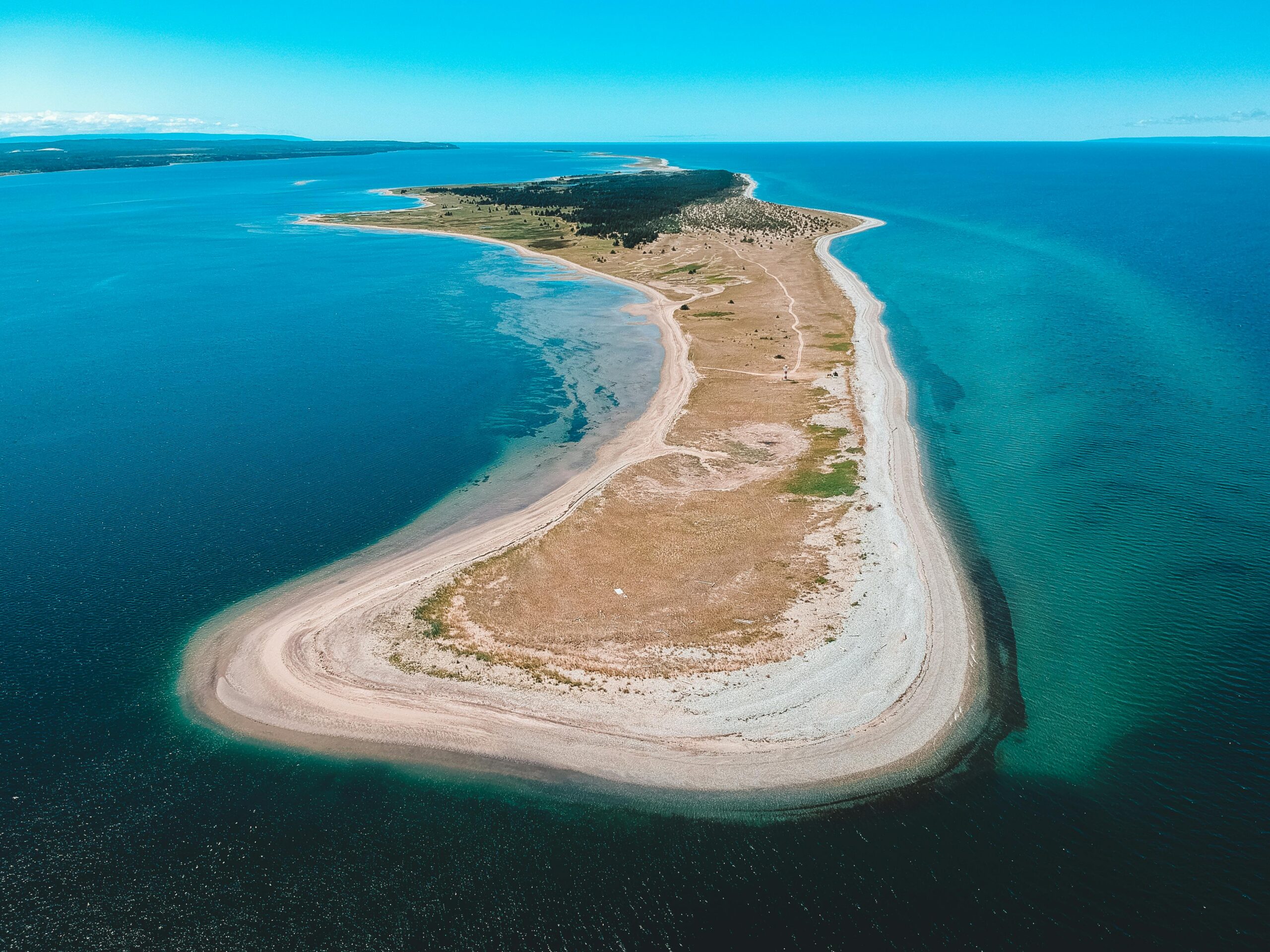 Drone view of sandy island with grass in blue sea under cloudy sky in daytime