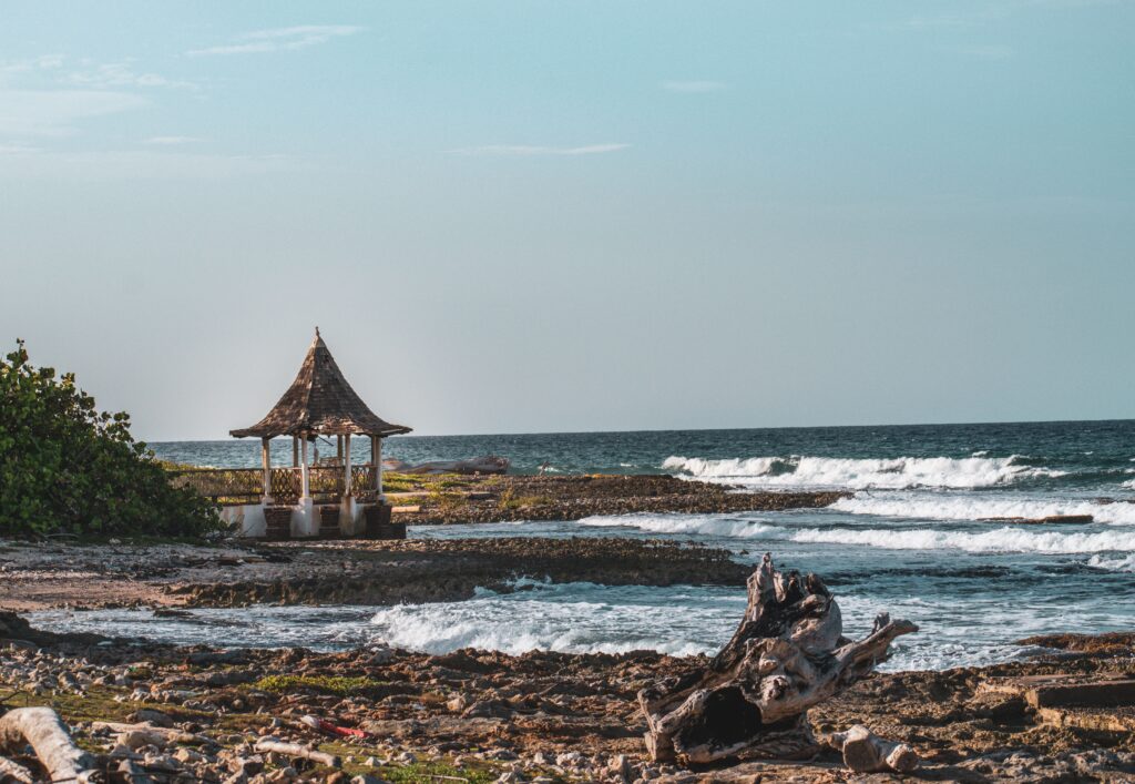 A picturesque beach scene with a gazebo by the sea, featuring waves crashing on a rocky shore.
