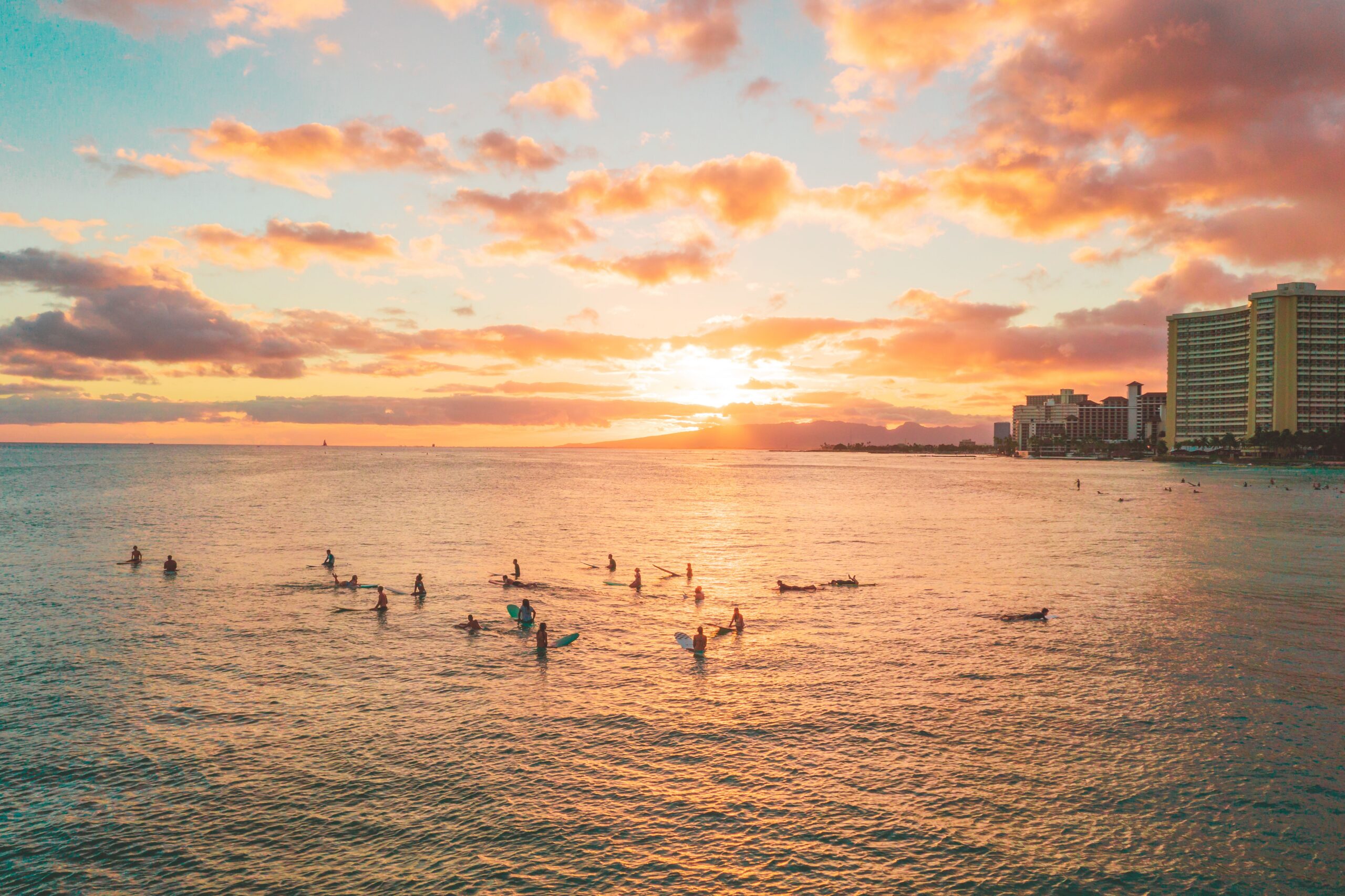Surfers enjoy the sunset at a Hawaiian beach, capturing the vibrant seascape and summer vibes.