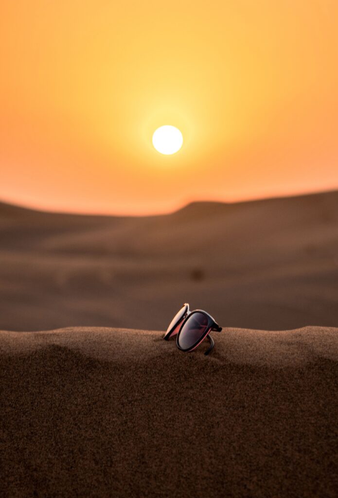 Scenic view of sunglasses on Dubai's desert sand with a stunning sunset backdrop.
