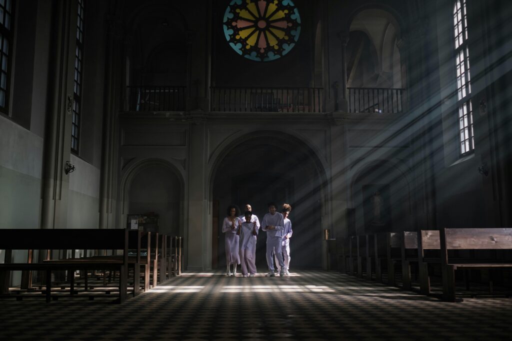 Choristers in uniforms sing under sunrays in a cathedral with stained glass.