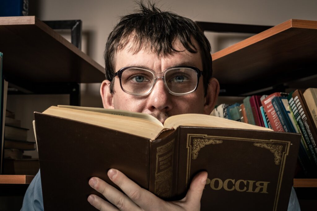 Man with glasses reading a book titled 'Россия' in a cozy library setting.