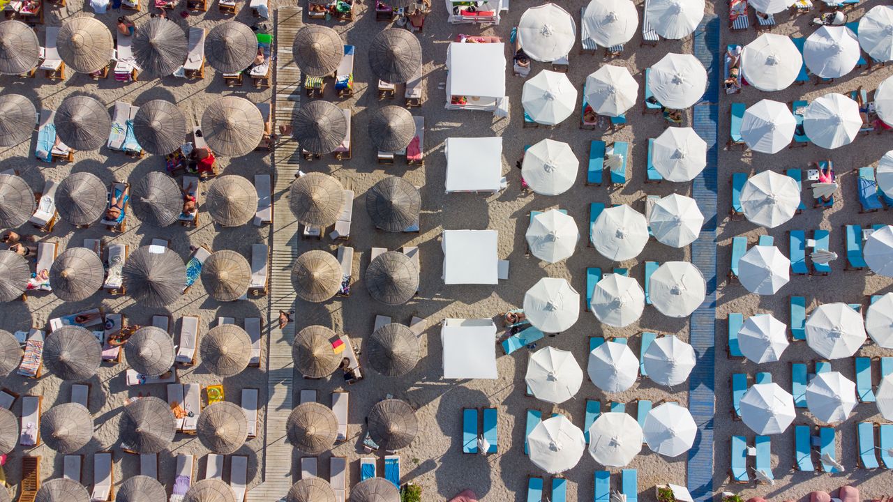 Aerial shot of beach umbrellas and sunbeds in Sarandë, Albania, during summer.