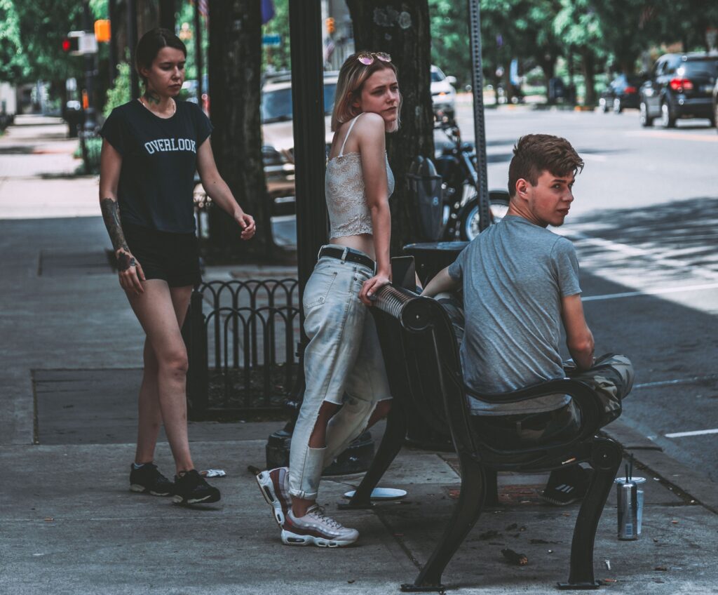 Group of trendy young adults relaxing on an urban street bench in casual wear during a sunny day.