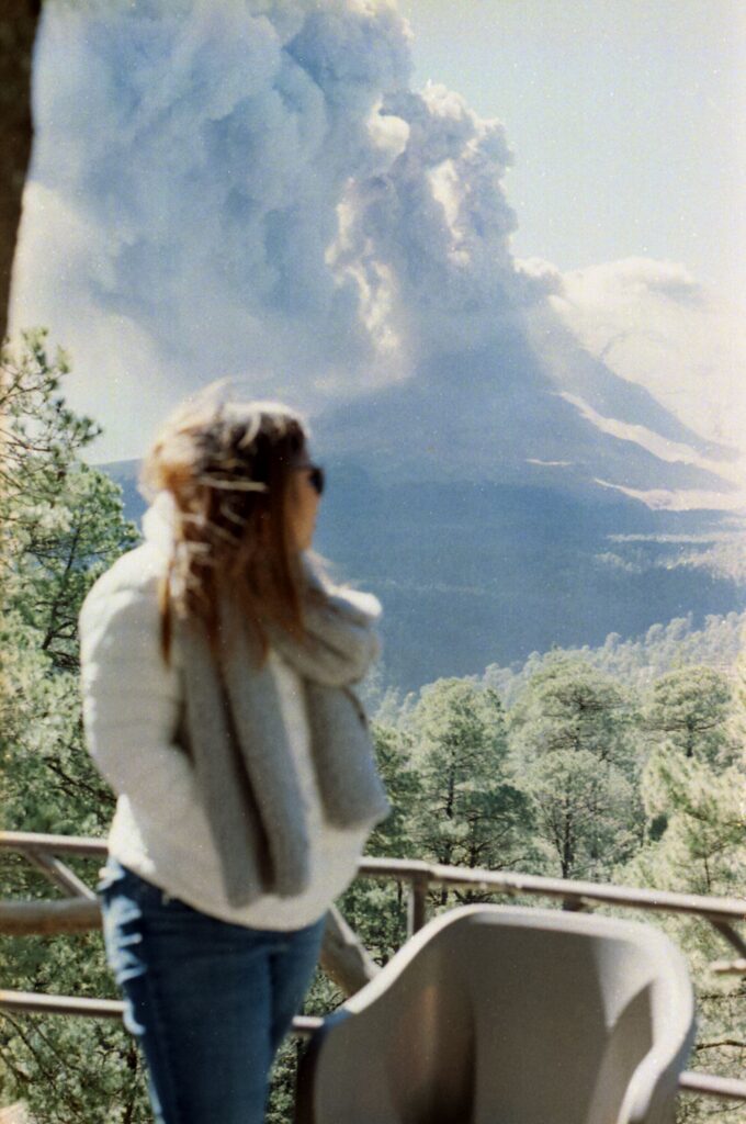 A woman watches an erupting volcano as it spews smoke and ash into the sky.