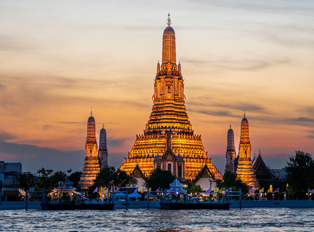 A captivating view of Wat Arun Temple illuminated at sunset along the Bangkok riverside.
