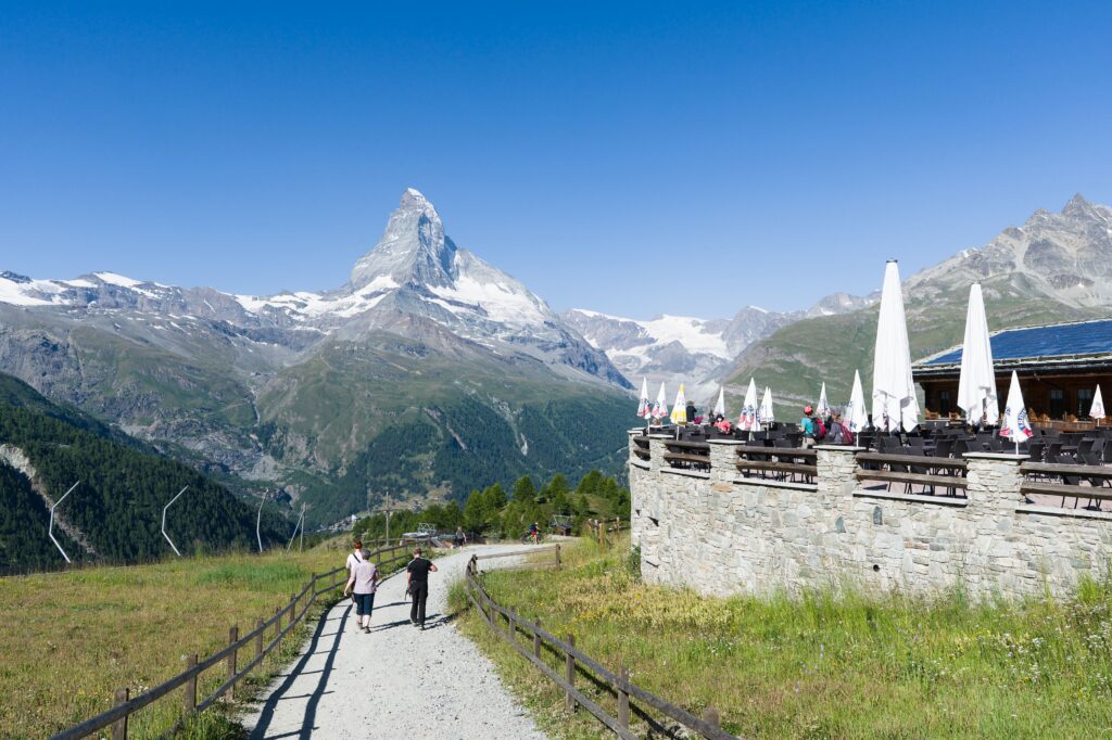 Tourists enjoy a sunny day at a mountain café with a breathtaking view of the Matterhorn in Switzerland.