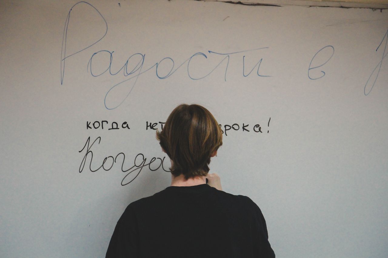 Person seen from behind writing Russian text on a wall in casual setting.