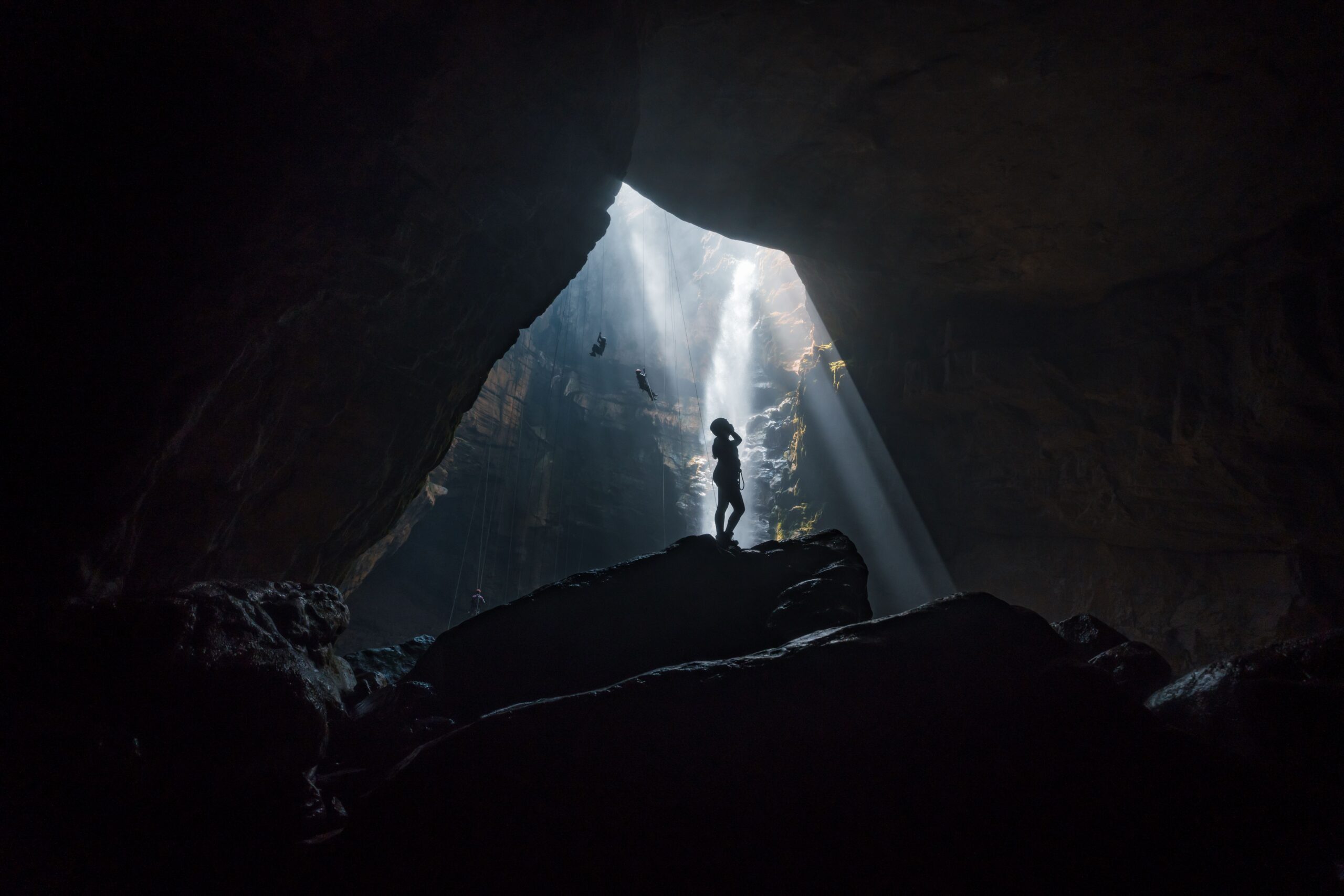 Silhouette of a person in a cave with dramatic light beams from above.