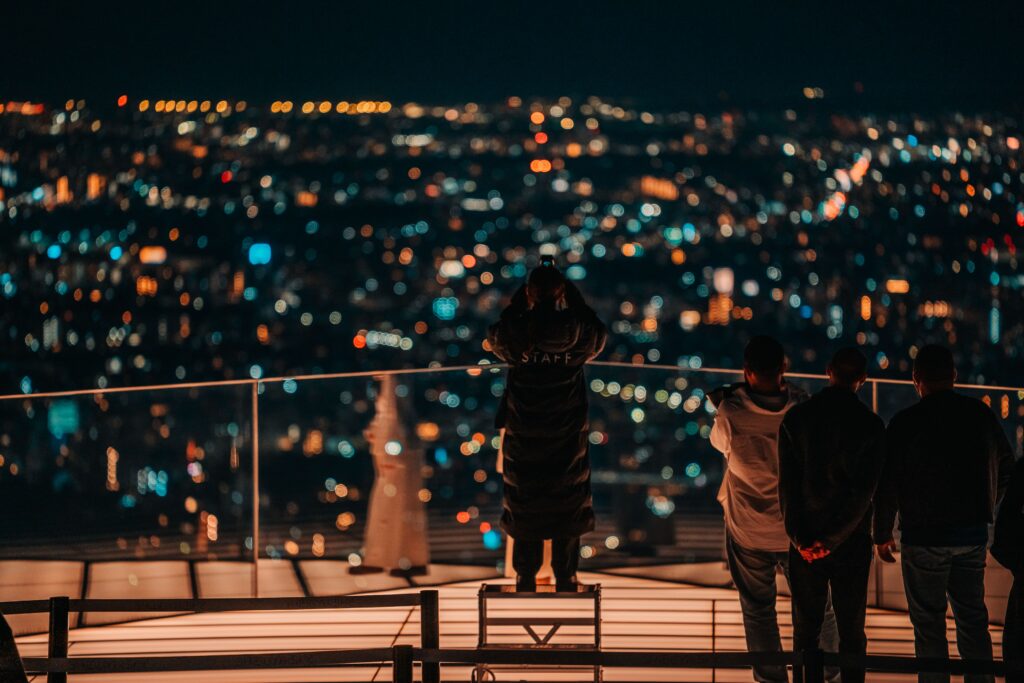 A group overlooking a vibrant nighttime cityscape from a rooftop in Shibuya, Tokyo.