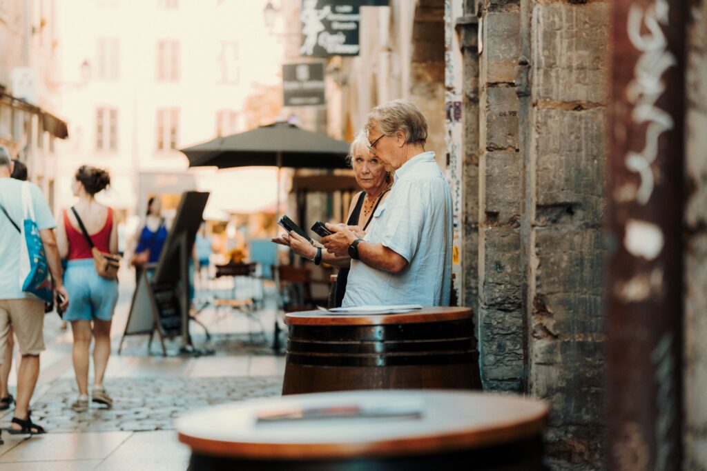 A senior couple examines their surroundings in a quaint European street setting.
