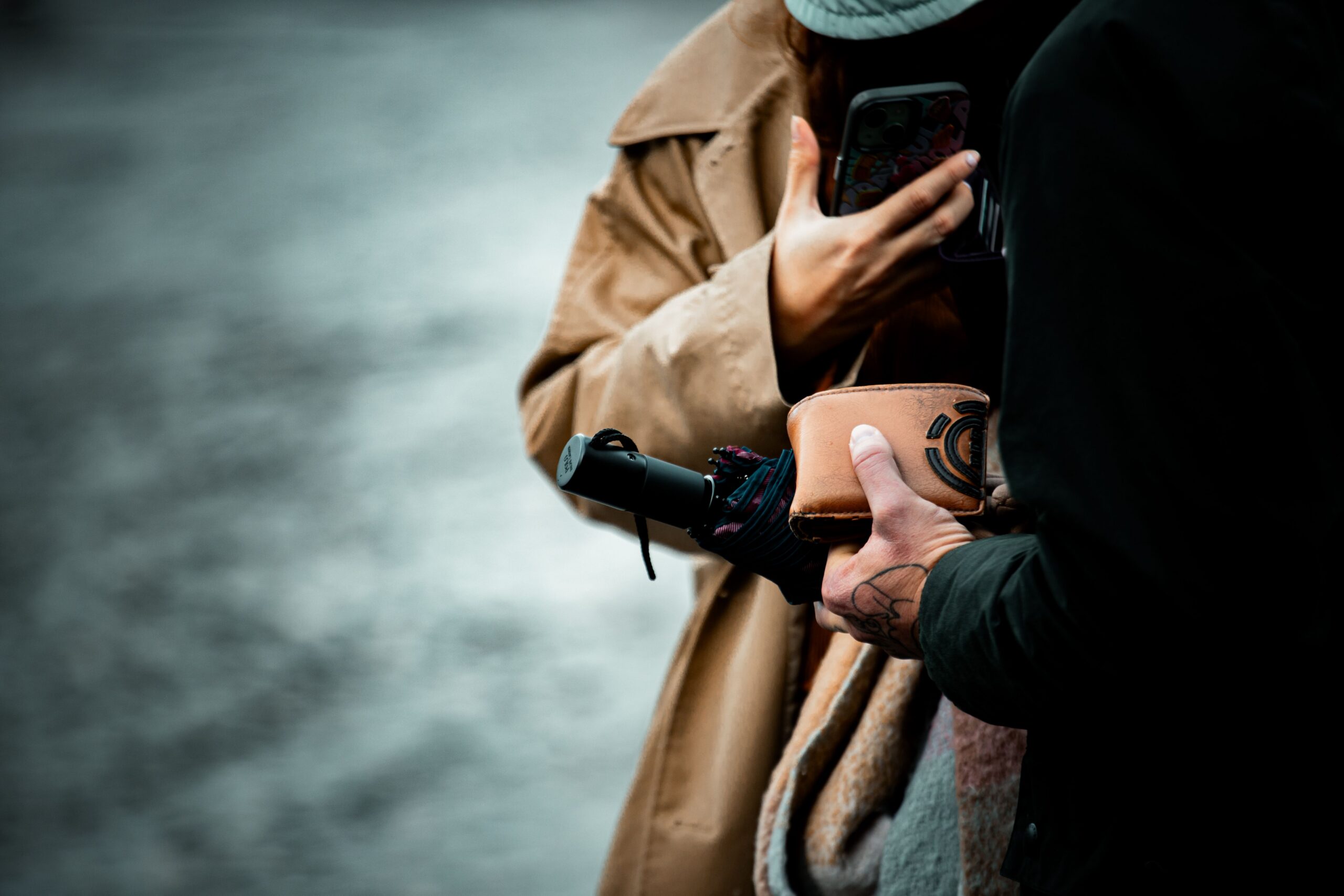 Close-up of urban interaction with a folded umbrella, wallet, and hand tattoo in fall attire.