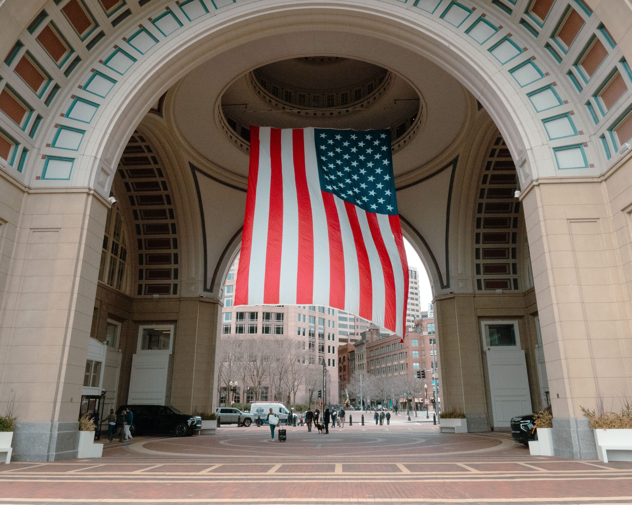 A large American flag hangs under an archway in Boston, capturing a patriotic urban scene.