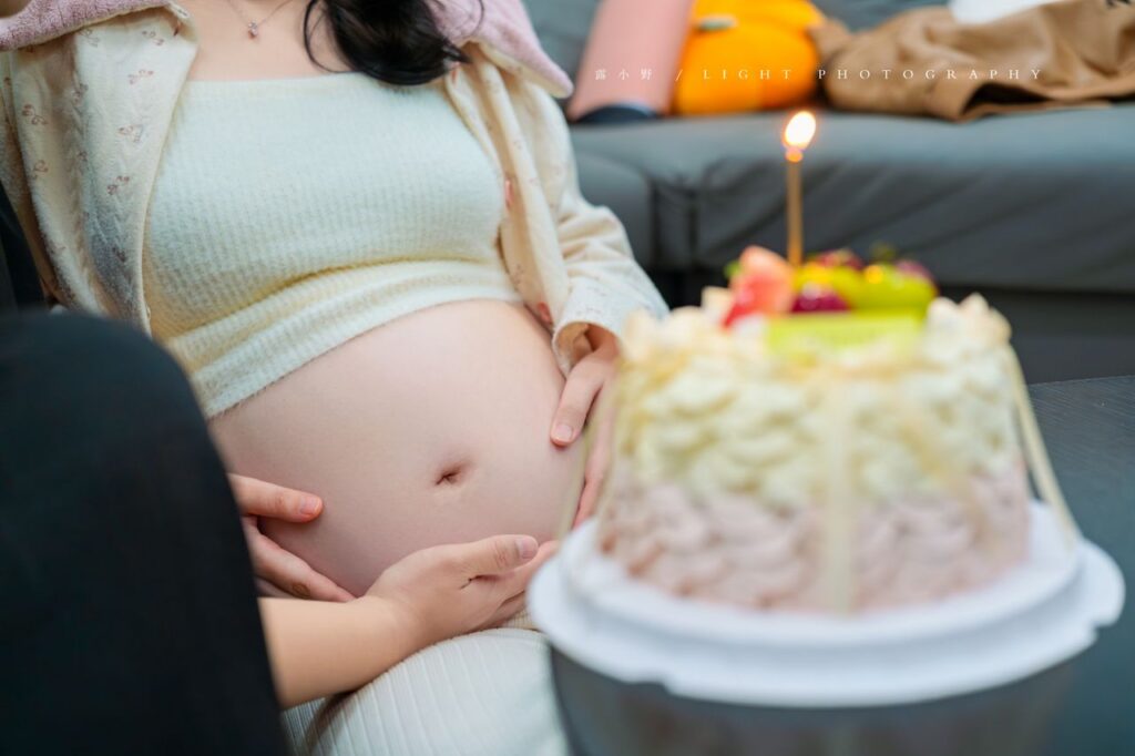 Pregnant woman caressing belly while a lit birthday cake is in the foreground.